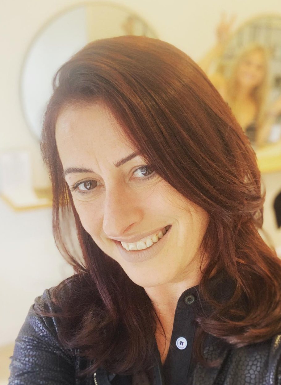 Christa Loisel, hair cutting and colour specialist, smiling in the salon with her glossy auburn hair